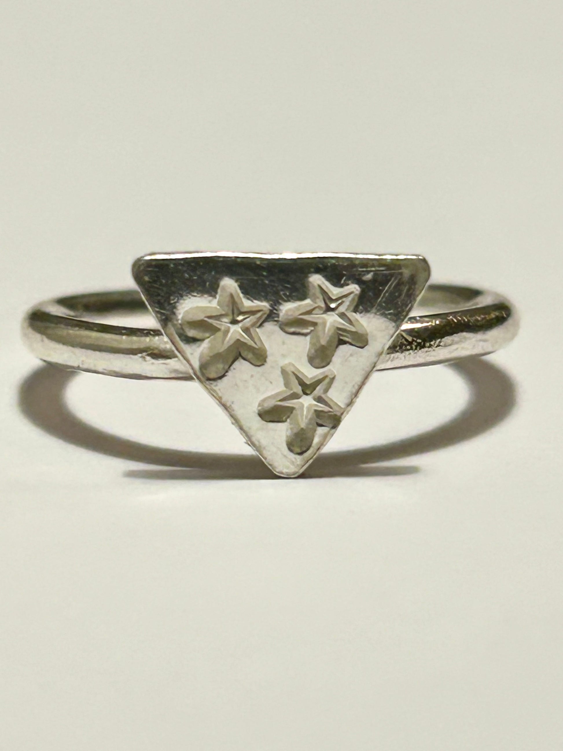 Silver ring with a triangular design featuring three stars on a light gray background